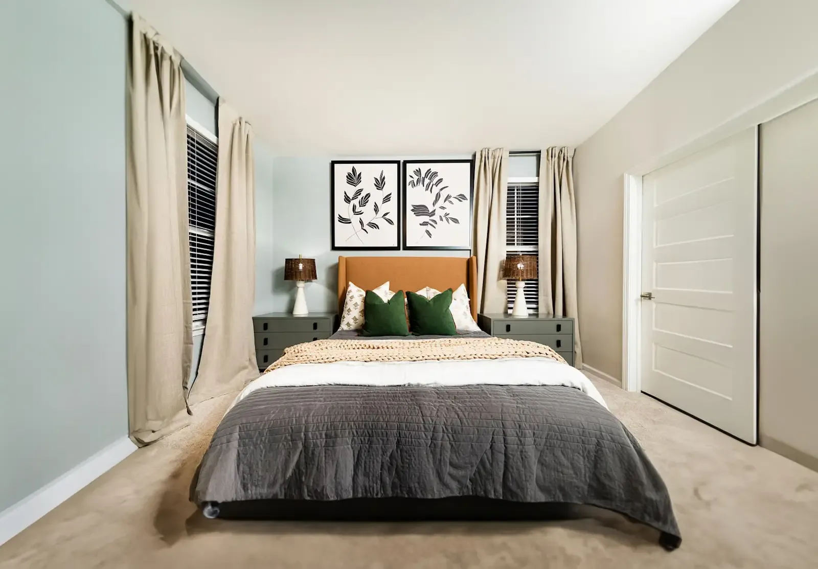 Modern bedroom at Evolve St. James with a cozy bed, neutral tones, and large windows with floor-length curtains.